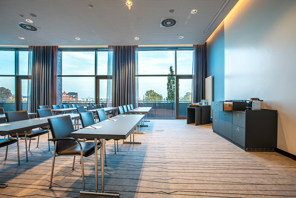 Fotoaufnahme des Meetingsraums Warnowblick 7 mit Stühlen und Tischen die zu einem Whiteboard ausgeirchtet sind